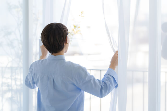 朝窓のカーテンを開ける女性画像